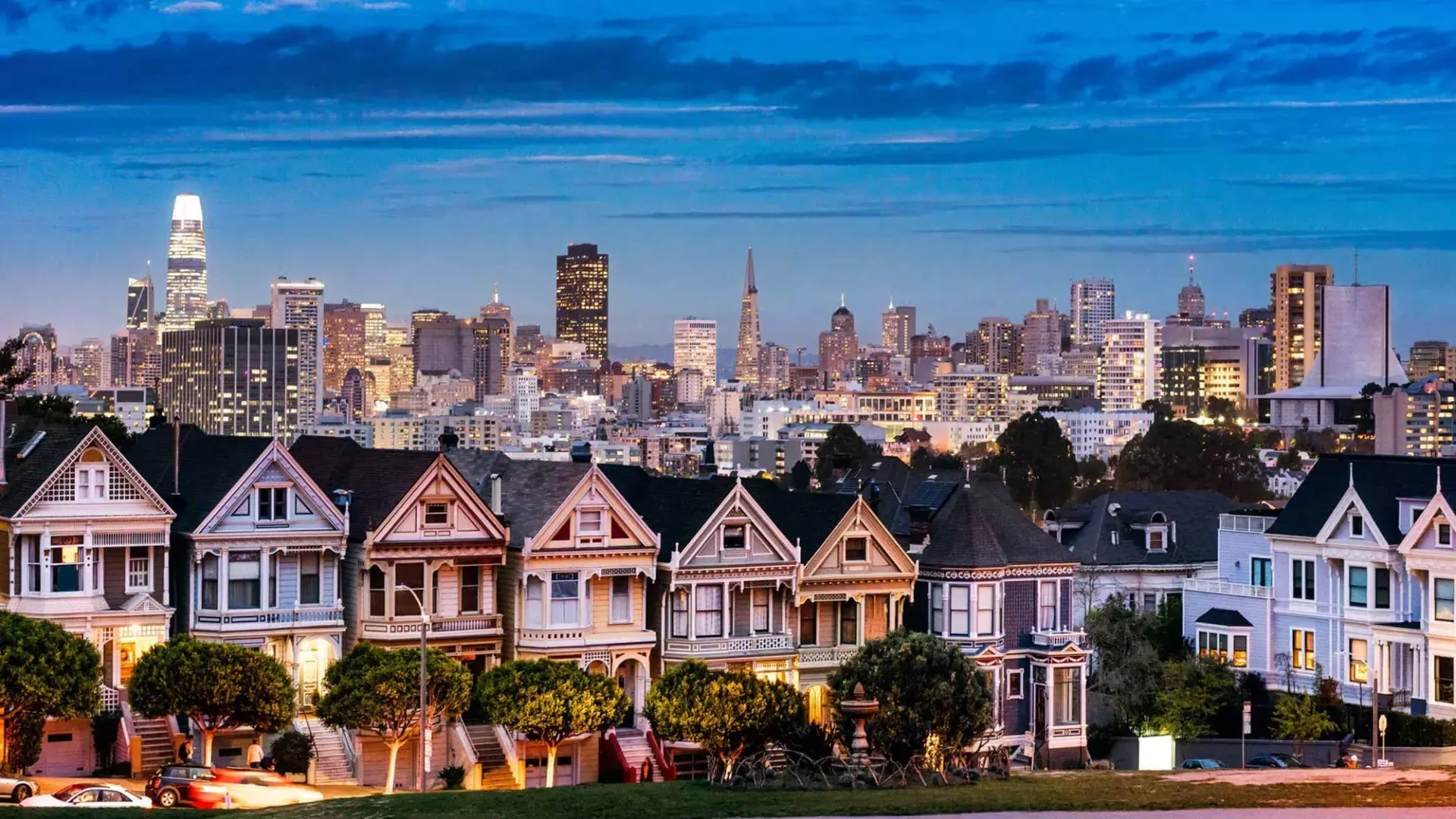 Die berühmten Painted Ladies vom Alamo Square sind in der Dämmerung vor der Skyline von San Francisco zu sehen.